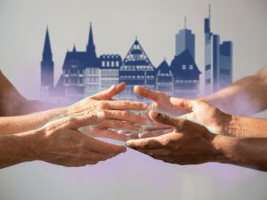 Diverse hands reaching toward each other in welcoming gesture with German architecture silhouettes in background