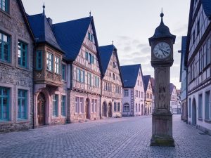 Traditional German stone buildings with peaked roofs, turquoise window frames, and cobblestone streets in morning light.