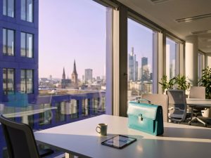 Turquoise briefcase on modern office desk with German cityscape visible through windows, featuring blue architecture and church spires